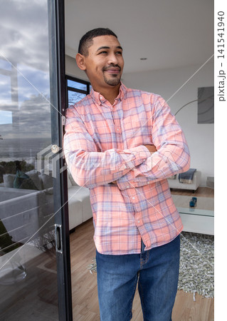 Mid adult man leaning against sliding glass door, gazing toward horizon from balcony, copy space 141541940