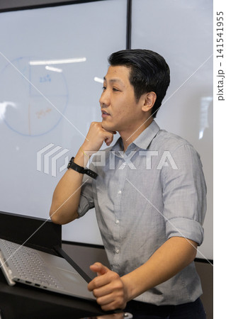 Asian man leading discussion in modern meeting room with laptop and pie chart on whiteboard Asian man leading discussion in modern meeting room with laptop and pie chart on whiteboard 141541955