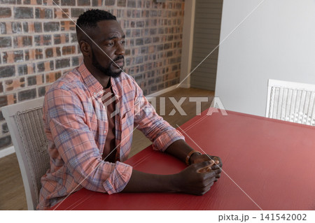 African american man sitting on white wicker chair against exposed brick wall gazing at table 141542002