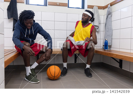 African american basketball players on locker room bench tying shoes, picking up basketball African american basketball players on locker room bench tying shoes, picking up basketball 141542039