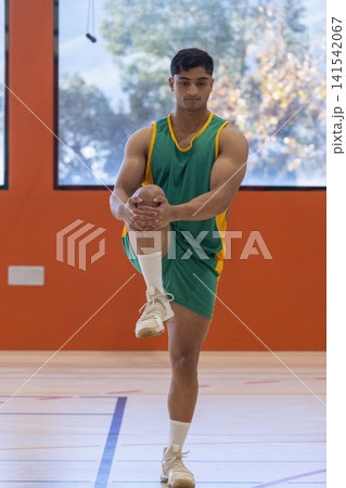 Man stretching on one leg pulling knee toward chest in gym on court 141542067