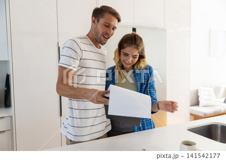 Couple standing at kitchen island reading printed document beside coffee mug and sink faucet Couple standing at kitchen island reading printed document beside coffee mug and sink faucet 141542177
