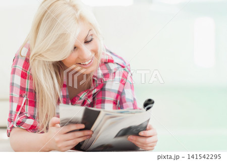 Woman reclining on pale sofa reading glossy magazine wearing red plaid shirt with rolled sleeves 141542295