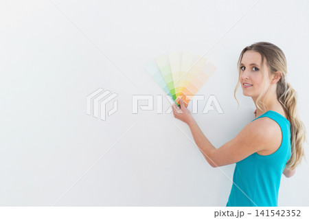 Woman in teal top holding paint swatches against white wall while standing in room, copy space Woman in teal top holding paint swatches against white wall while standing in room, copy space 141542352