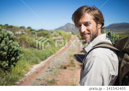 Bearded man standing on right of sunlit dirt track with backpack straps visible, copy space Bearded man standing on right of sunlit dirt track with backpack straps visible, copy space 141542405