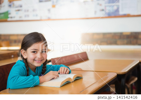 Child female student sitting in classroom at desk reading book, wearing turquoise top, copy space Child female student sitting in classroom at desk reading book, wearing turquoise top, copy space 141542416