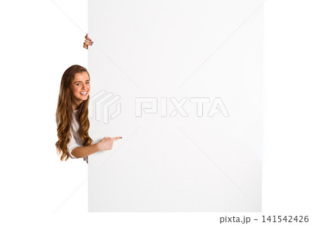 Woman peeking left in studio, pointing at blank white panel in white long-sleeve top, copy space Woman peeking left in studio, pointing at blank white panel in white long-sleeve top, copy space 141542426