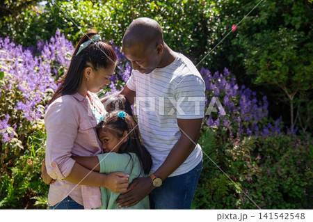 Diverse family embracing in backyard garden surrounded by green foliage and purple flowering shrubs Diverse family embracing in backyard garden surrounded by green foliage and purple flowering shrubs 141542548