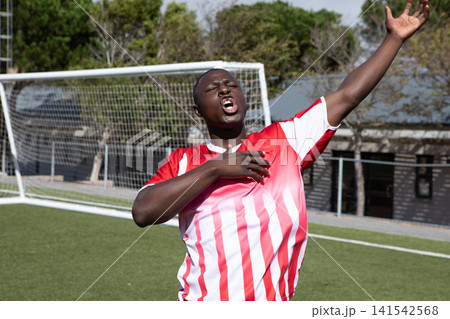 African American male soccer player celebrating on artificial turf by goal net in red uniform 141542568
