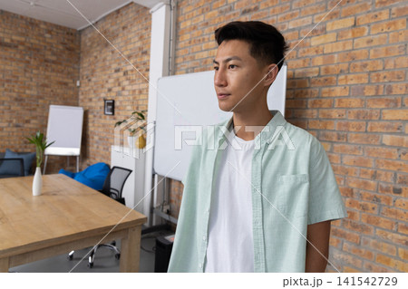 Asian male standing beside brick wall in meeting room with table and whiteboard, copy space Asian male standing beside brick wall in meeting room with table and whiteboard, copy space 141542729