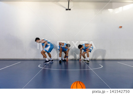 Three african american men in uniforms squatting under hoop on court with orange basketball Three african american men in uniforms squatting under hoop on court with orange basketball 141542750