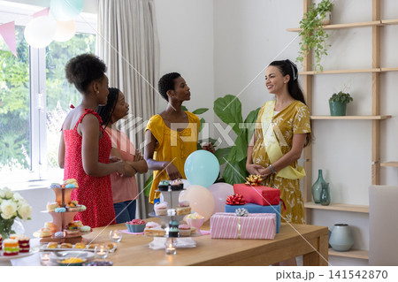 Diverse female friends gathering around table in dining area with cupcakes and candles, copy space Diverse female friends gathering around table in dining area with cupcakes and candles, copy space 141542870