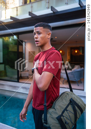 Male in mid-20s standing by pool edge on pool deck with duffel bag, smartwatch, copy space Male in mid-20s standing by pool edge on pool deck with duffel bag, smartwatch, copy space 141542949