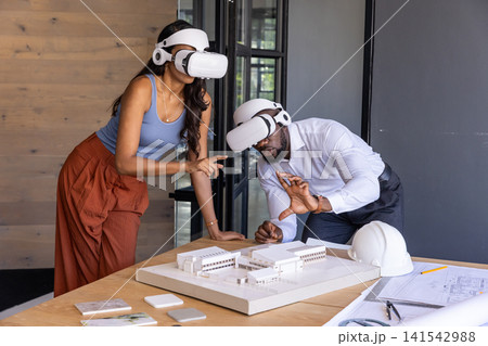 Diverse colleagues wearing vr headsets pointing at scale model blueprints in design studio Diverse colleagues wearing vr headsets pointing at scale model blueprints in design studio 141542988