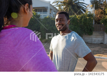Diverse friends pausing mid run and chatting on suburban sidewalk by hedge 141543175