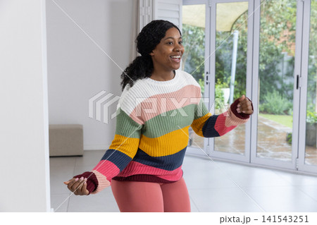 African american woman exercising at home on tiled floor next to ottoman bench and sliding door African american woman exercising at home on tiled floor next to ottoman bench and sliding door 141543251