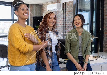 Diverse female coworkers talking and smiling while working at open office space with monitors Diverse female coworkers talking and smiling while working at open office space with monitors 141543364