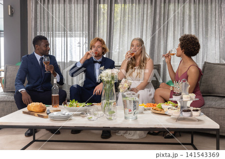 Diverse wedding party sitting on grey couch in lounge sipping ros��, dessert stand Diverse wedding party sitting on grey couch in lounge sipping ros��, dessert stand 141543369