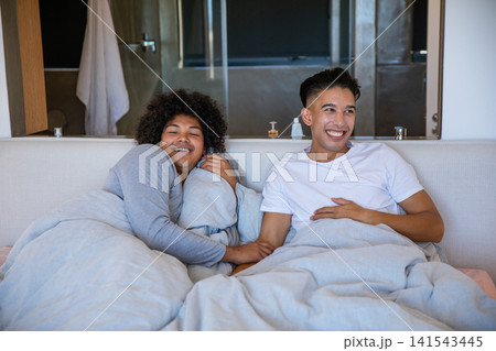 Diverse male partners lying under duvet in bedroom with mirror showing soap dispenser and lotion Diverse male partners lying under duvet in bedroom with mirror showing soap dispenser and lotion 141543445