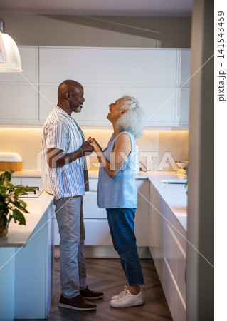 Diverse couple standing holding hands and gazing at each other in kitchen with countertop island Diverse couple standing holding hands and gazing at each other in kitchen with countertop island 141543459