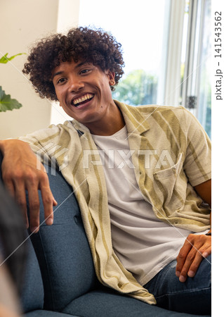 Man sitting on sofa in bright living room beside potted plant near sliding glass door Man sitting on sofa in bright living room beside potted plant near sliding glass door 141543562