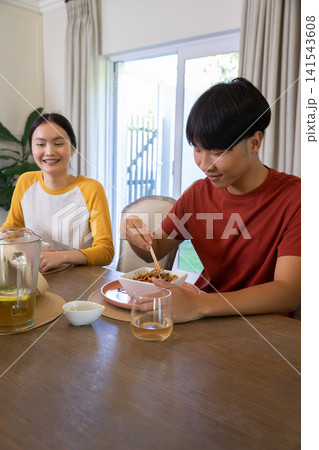 Asian couple eating noodles using chopsticks at home dining table with pitcher of beverage 141543608