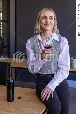 Female drinking red wine beside wine bottle on table in modern tasting room Female drinking red wine beside wine bottle on table in modern tasting room 141543729