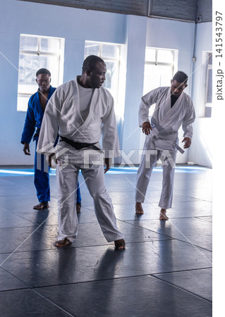 African american men practicing footwork drills in gis with belts on mats by windows African american men practicing footwork drills in gis with belts on mats by windows 141543797
