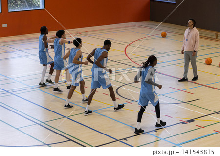 Diverse male basketball team shuffling in footwork drill on court lines near coach whistle 141543815