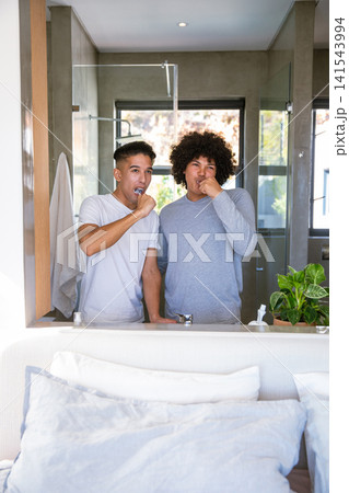 Male friends in loungewear brushing teeth at modern home bathroom sink mirror with toothbrushes Male friends in loungewear brushing teeth at modern home bathroom sink mirror with toothbrushes 141543994