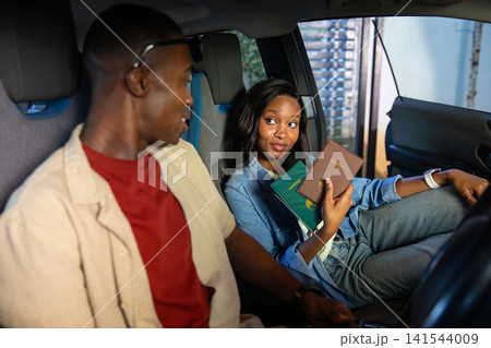 African American couple holding passports and talking inside parked car near metal shutter 141544009