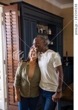 Diverse couple leaning on wood countertop with glass spice jars gazing off to side in the kitchen Diverse couple leaning on wood countertop with glass spice jars gazing off to side in the kitchen 141544148