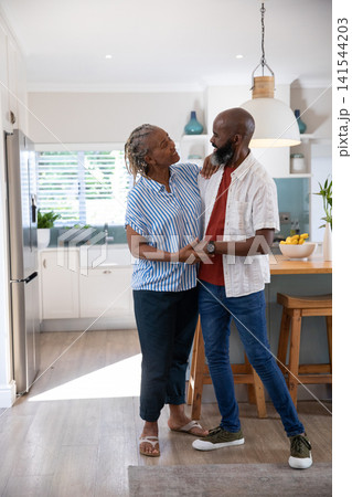 Senior African American couple standing in modern kitchen with banana bowl on island, holding hands 141544203