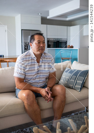 Middle-aged chinese man sitting on sofa in living room with coffee table and wooden logs 141544239