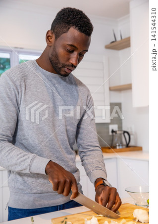 African american man slicing cauliflower florets holding chef's knife on cutting board in kitchen African american man slicing cauliflower florets holding chef's knife on cutting board in kitchen 141544310