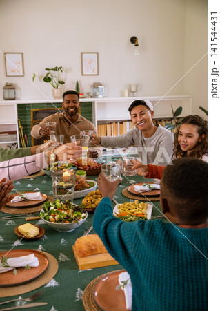 Diverse friends raising glasses and sharing roast turkey dinner at wooden table with cloth 141544431