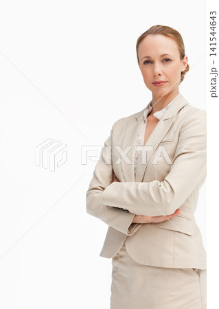 Mid-30s woman standing with arms crossed in studio wearing beige blazer and skirt, copy space 141544643