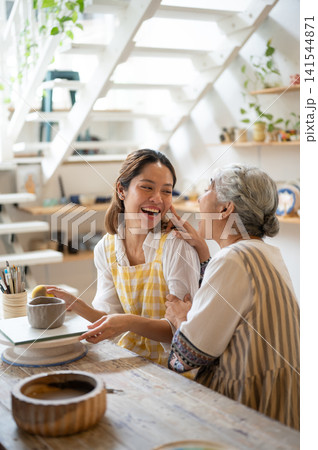 Senior Mother Touching Laughing Daughter's Face during a Pottery Class in art workshop. Senior Mother Touching Laughing Daughter's Face during a Pottery Class in art workshop. 141544871