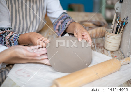 Close Up of Senior Woman Hands Holding Flat Clay Disc for Plate Making in pottery workshop studio Close Up of Senior Woman Hands Holding Flat Clay Disc for Plate Making in pottery workshop studio 141544906