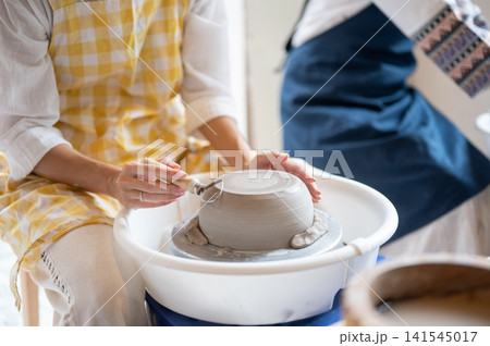 Close up of woman's hands shaping clay on pottery wheel creating a handmade ceramic bowl in workshop Close up of woman's hands shaping clay on pottery wheel creating a handmade ceramic bowl in workshop 141545017