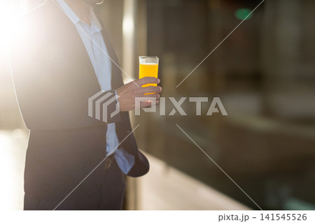 Midadult man in dark suit shirt standing holding orange juice glass in office lobby, copy space Midadult man in dark suit shirt standing holding orange juice glass in office lobby, copy space 141545526