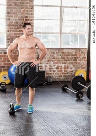 Bare-chested muscular man standing in gym near kettlebell and barbell, wearing black shorts Bare-chested muscular man standing in gym near kettlebell and barbell, wearing black shorts 141545556