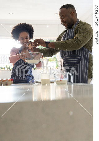 African American couple in striped aprons making batter at kitchen island holding mixing bowl African American couple in striped aprons making batter at kitchen island holding mixing bowl 141546207