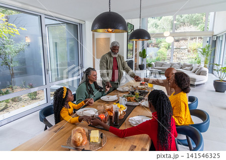 African American multigenerational family holding hands around dining table at home with bread African American multigenerational family holding hands around dining table at home with bread 141546325