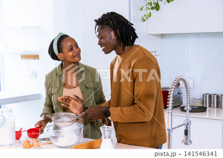 African American couple preparing baking at kitchen island with glass bowl, sifter, eggs, milk African American couple preparing baking at kitchen island with glass bowl, sifter, eggs, milk 141546341