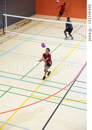 Diverse male players with Asian teen preparing forearm pass, playing on hardwood gym court near net 141546498
