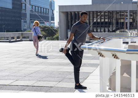 Diverse people, one in gym gear stretching at roof railing, woman walking holding phone, copy space 141546513