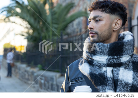 Man standing on city sidewalk holding white takeaway cup and wearing checkered scarf, copy space Man standing on city sidewalk holding white takeaway cup and wearing checkered scarf, copy space 141546519