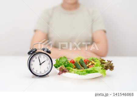 happy smiling woman with fresh organic vegetables plate and alarm clock. intermittent fasting, IF, meal time, nutrition, weight loss, clean eating, Healthy food eating, Wellness, dieting and lifestyle happy smiling woman with fresh organic vegetables plate and alarm clock. intermittent fasting, IF, meal time, nutrition, weight loss, clean eating, Healthy food eating, Wellness, dieting and lifestyle 141546868