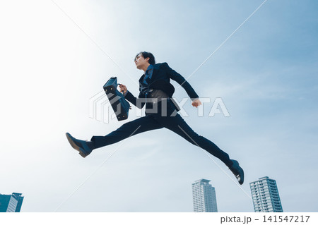 青空を背景にジャンプをするビジネスマン 青空を背景にジャンプをするビジネスマン 141547217